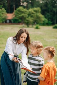 Woman in White Long Sleeve Shirt Showing a Book to a Boy and Girl